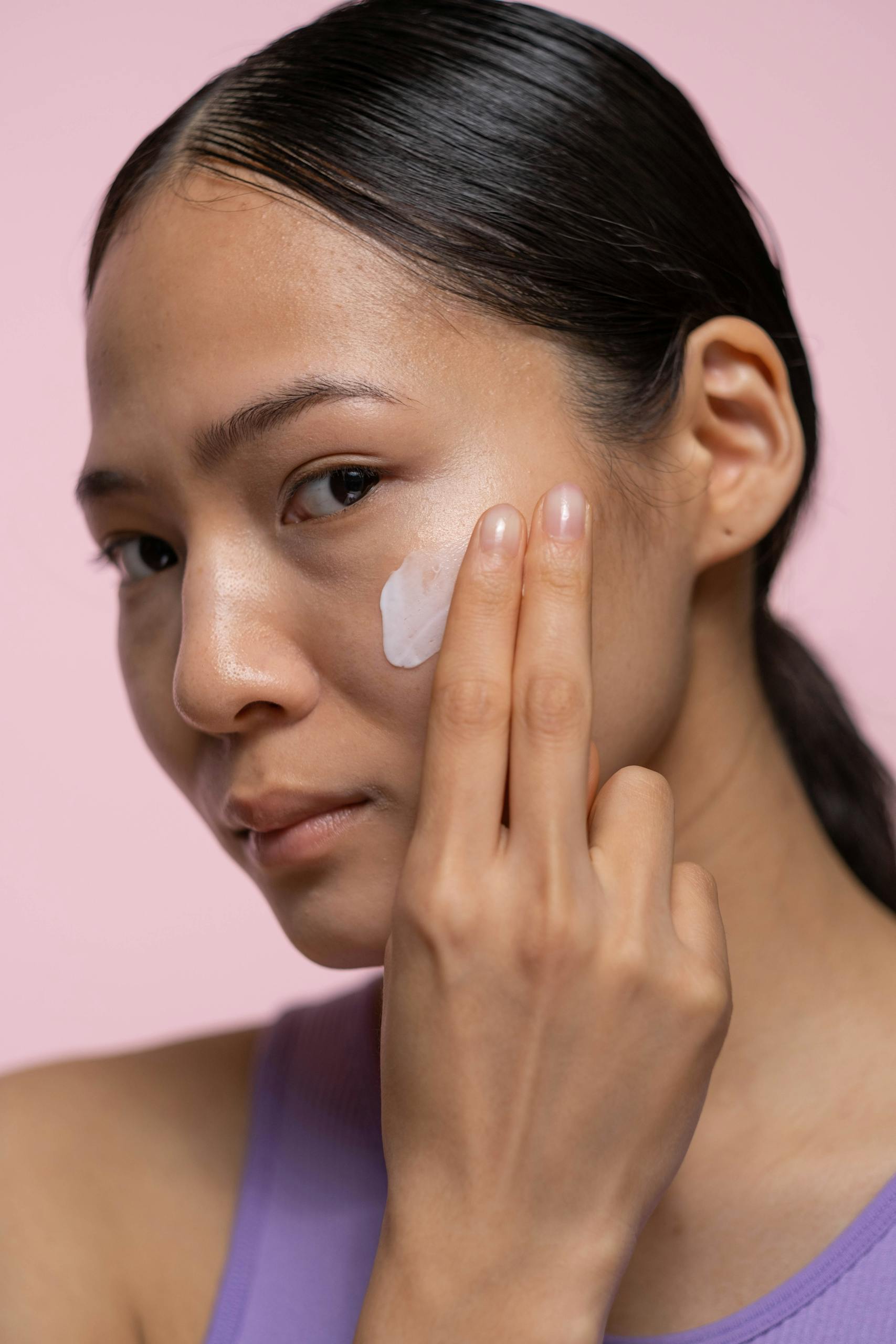 Close-up of a woman applying skincare cream indoors.